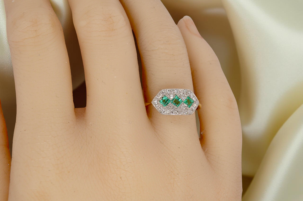 hand fine Edwardian era cluster ring, beautifully handcrafted with a trio of vibrant emeralds surrounded by a halo of antique old-cut diamonds.