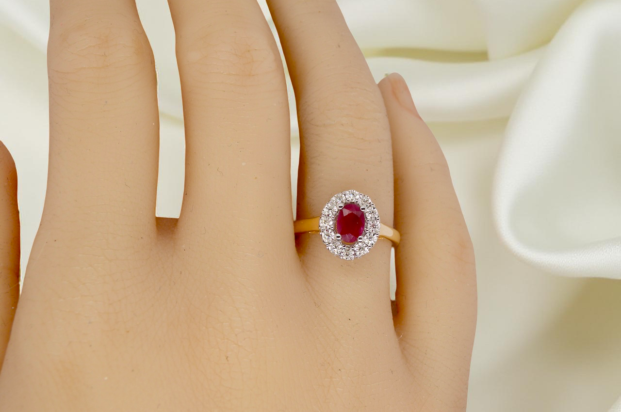 hand oval ruby measuring 6x4mm (approx. 0.44 carats) in a raspberry red hue. The centre stone is accented by a halo of twelve white diamonds