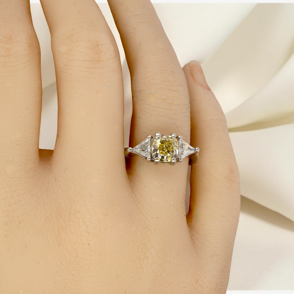 hand striking and elegant trilogy ring crafted in 18-carat white gold, set with a vibrant fancy yellow cushion-cut diamond