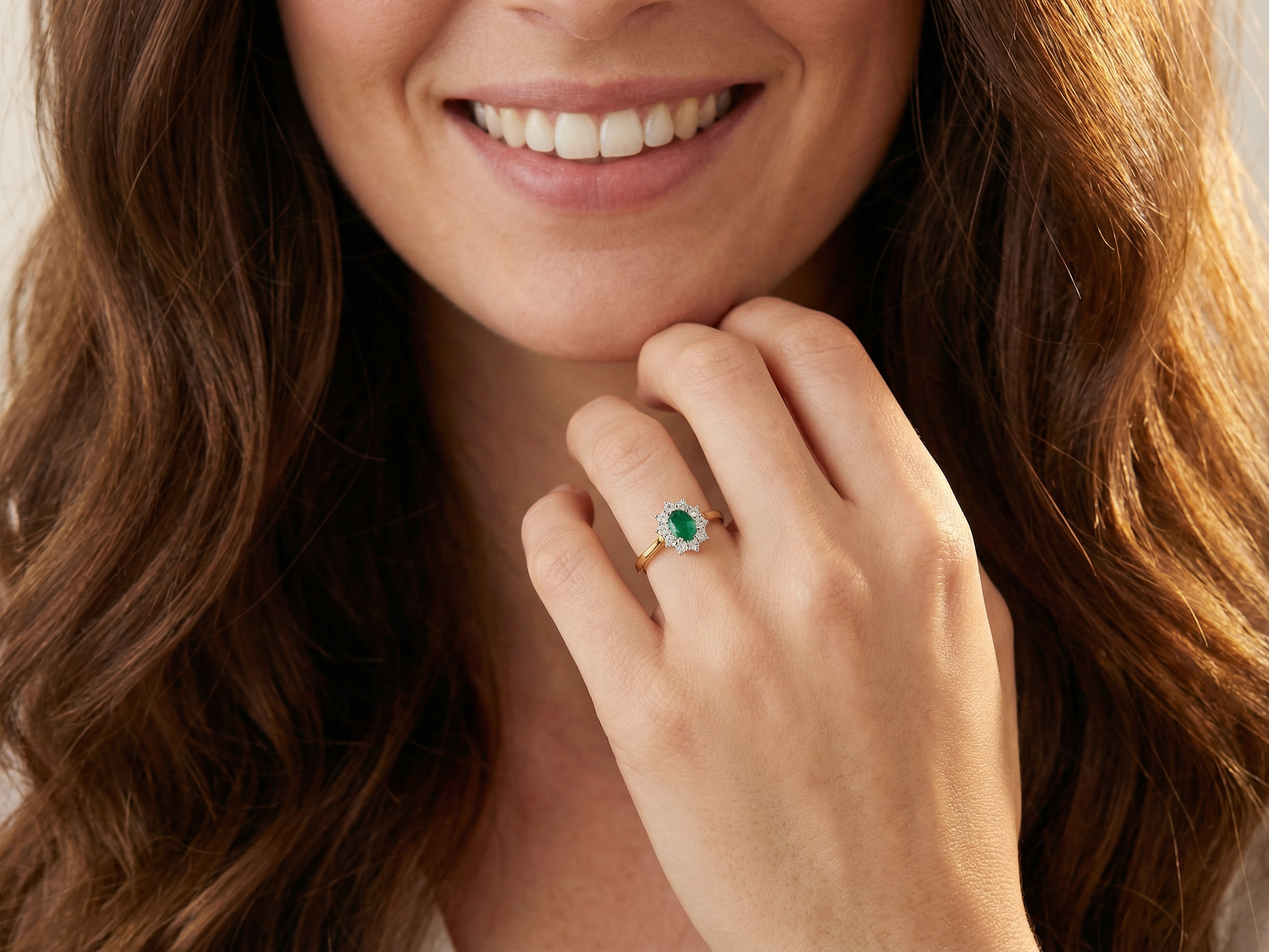 model A fine traditional emerald and diamond cluster ring, featuring a vibrant oval-cut emerald to the centre measuring approximately 7 × 5 mm