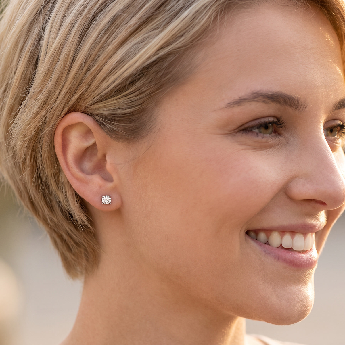 A close-up side profile of a smiling woman with short blonde hair wearing a small round stud earring.