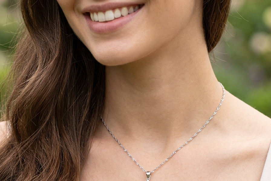 model A white gold pendant. The centre stone an inky black blue sapphire 7x5mm, claw set. Complimented by an outer halo of twelve brilliant cut white diamonds.