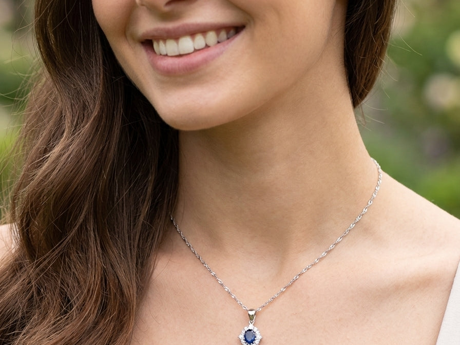 model A white gold pendant. The centre stone an inky black blue sapphire 7x5mm, claw set. Complimented by an outer halo of twelve brilliant cut white diamonds.