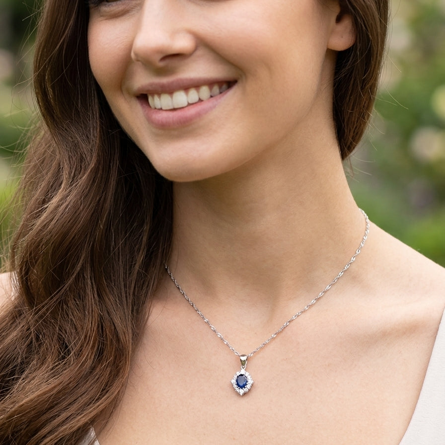 model A white gold pendant. The centre stone an inky black blue sapphire 7x5mm, claw set. Complimented by an outer halo of twelve brilliant cut white diamonds.