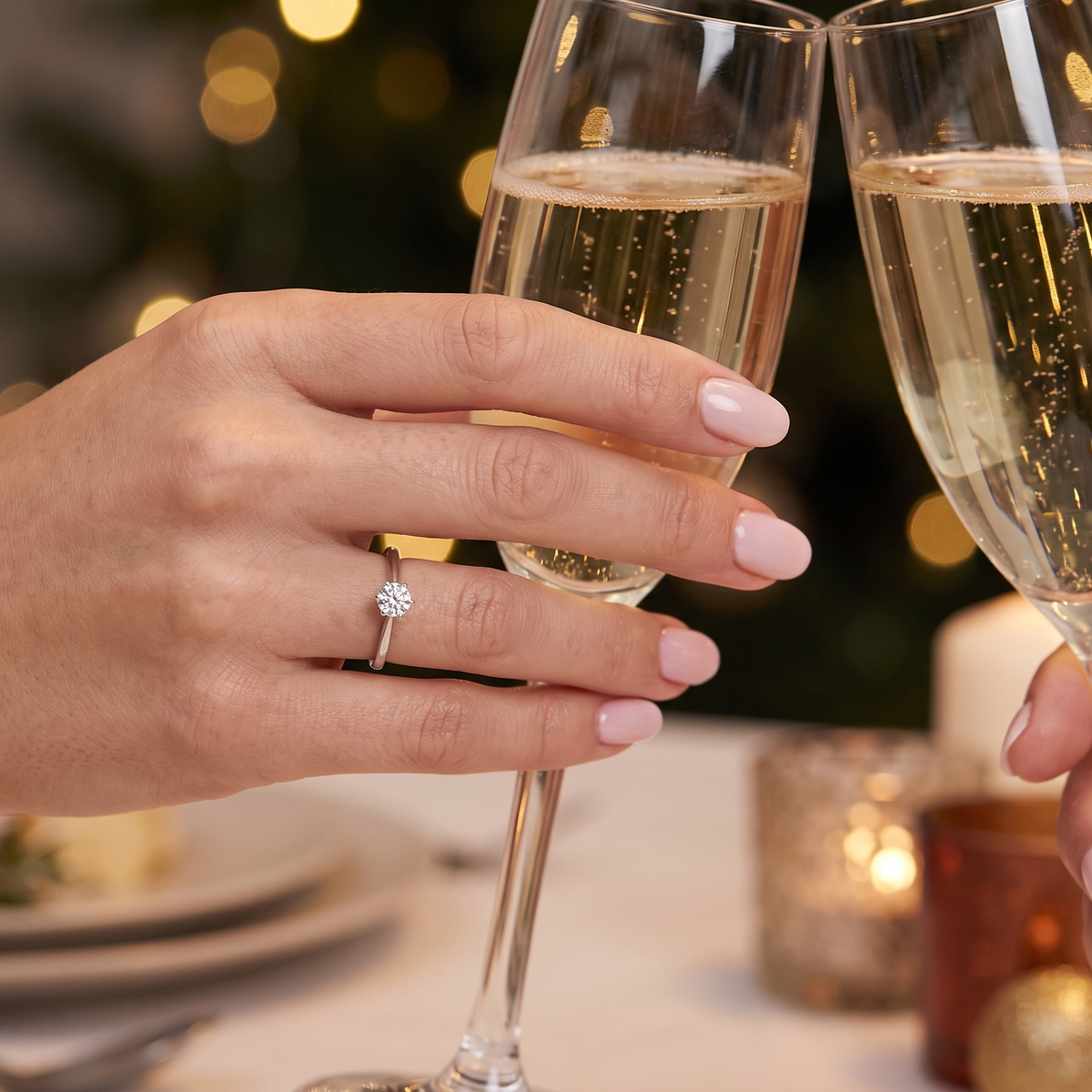 A close-up lifestyle shot of a person wearing a silver ring with a clear round gemstone, clinking champagne glasses at a dinner table with warm holiday bokeh lights in the background.