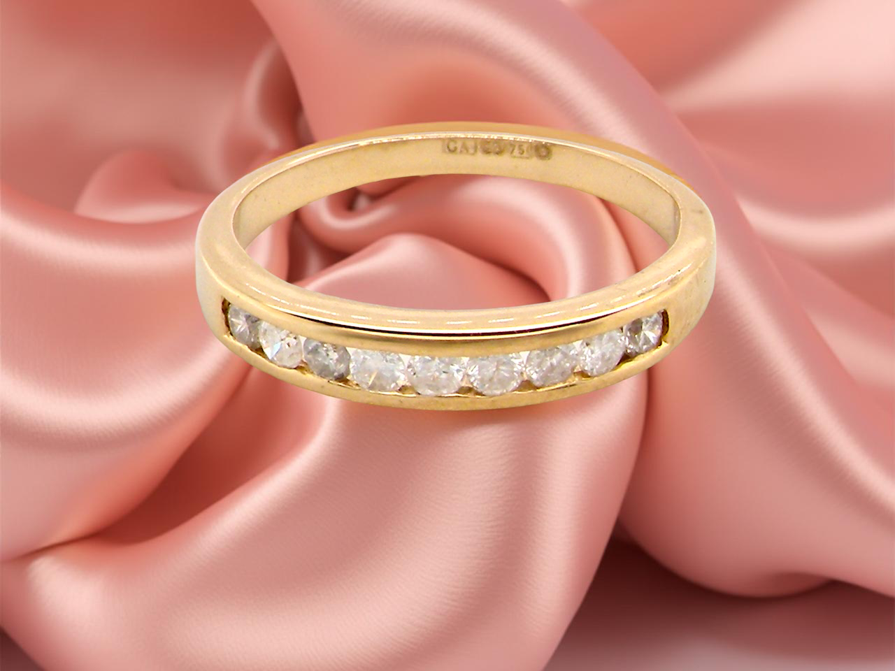 Gold ring with diamonds on a pink satin background