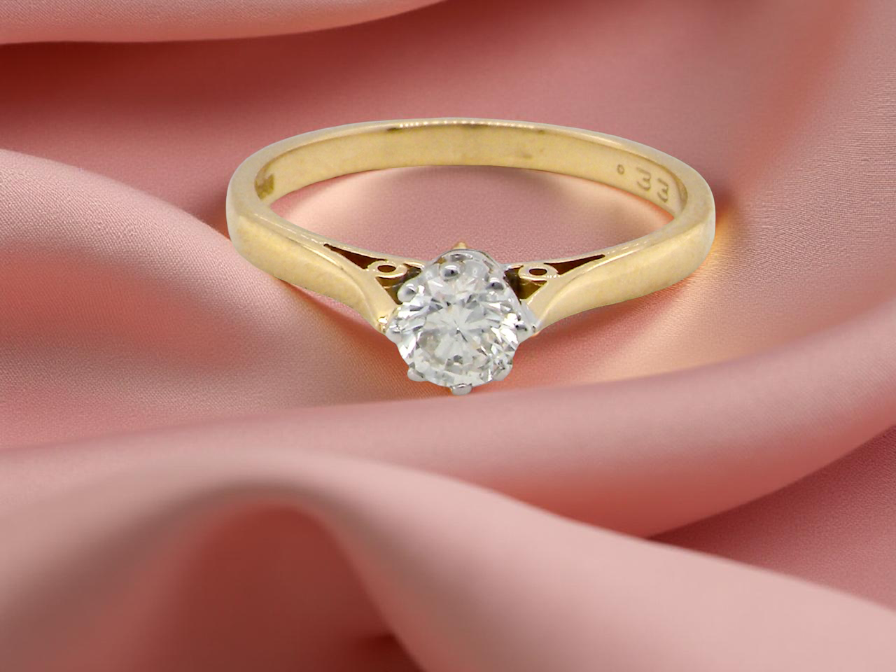 Gold ring with a diamond on a pink fabric background