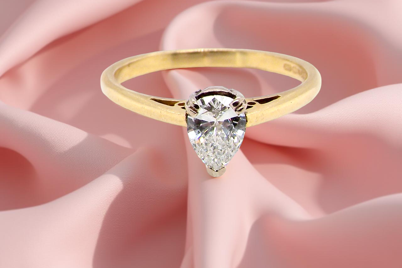Gold ring with a pear-shaped diamond on a pink fabric background