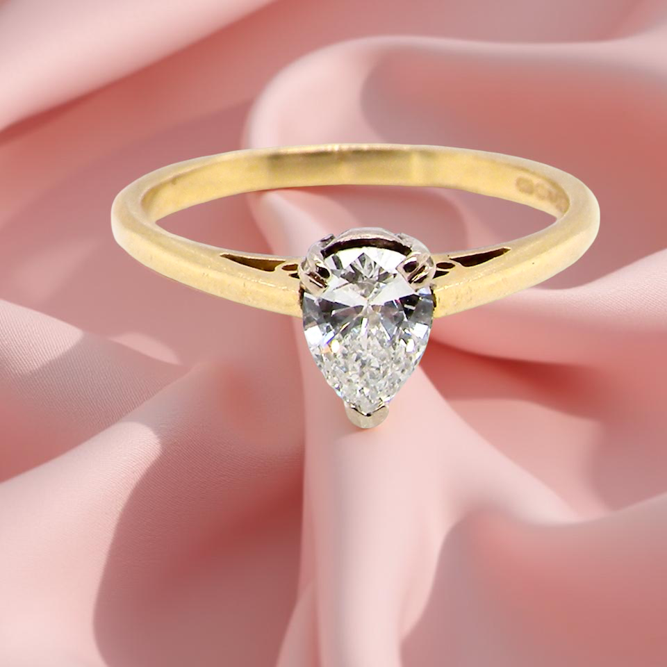 Gold ring with a pear-shaped diamond on a pink fabric background