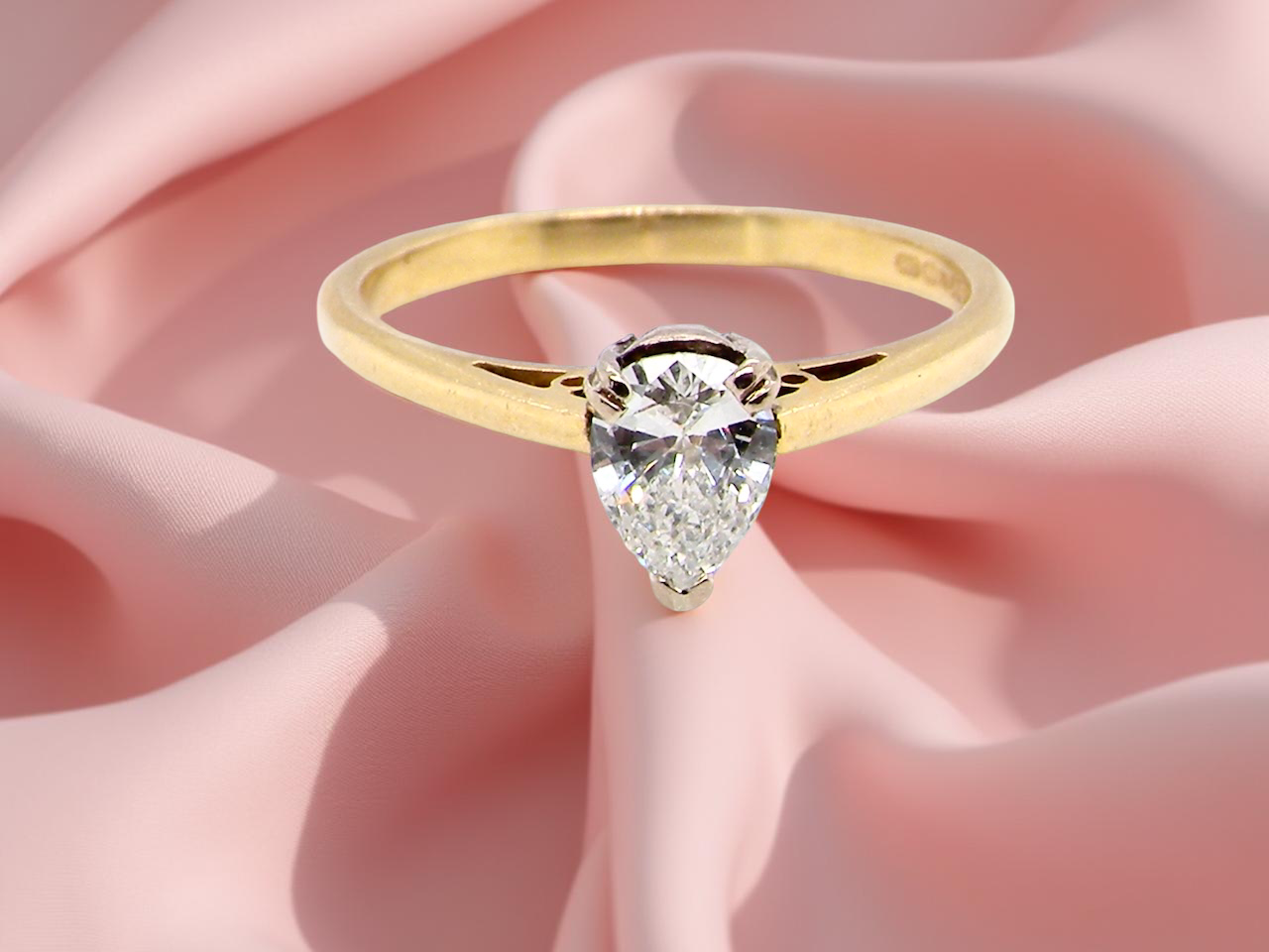 Gold ring with a pear-shaped diamond on a pink fabric background