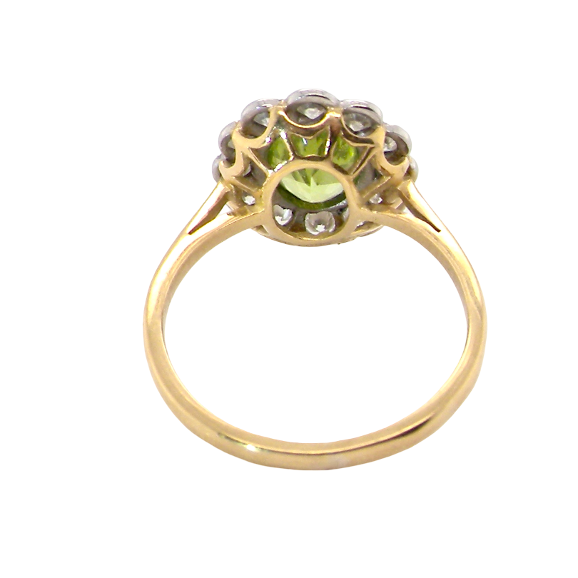 A yellow gold ring featuring a central light green peridot gemstone surrounded by small clear stones in a decorative setting, shown on a plain white background.