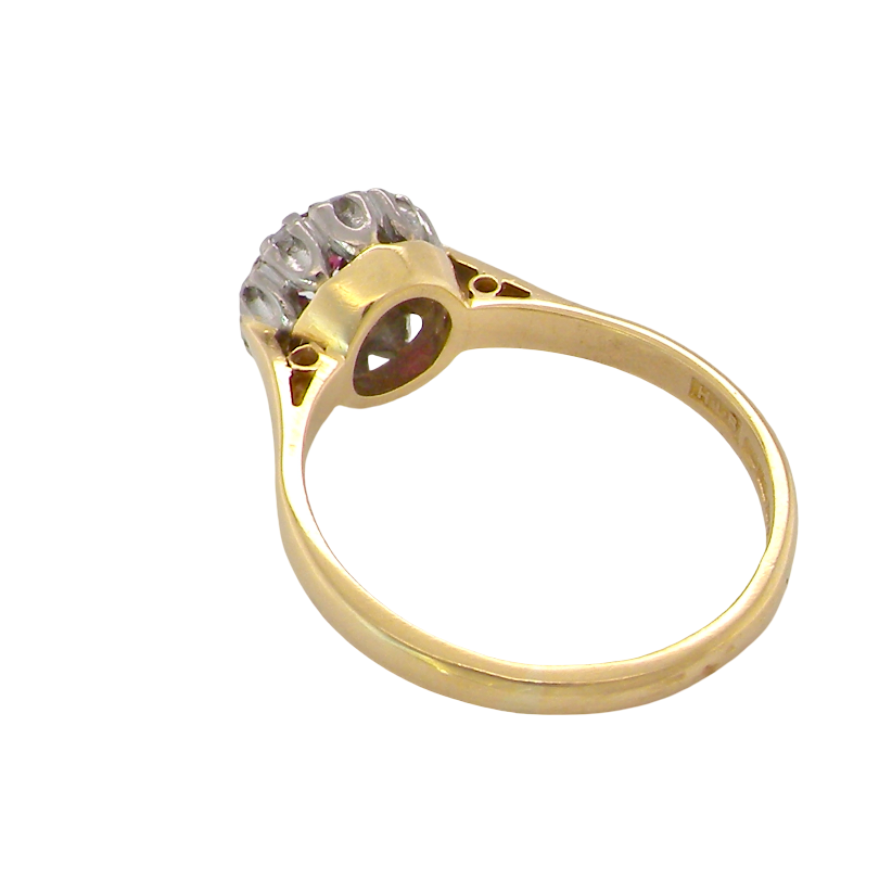 A yellow gold ring with a floral cluster setting featuring clear gemstones and a tiny red accent stone, shown on a plain white background.