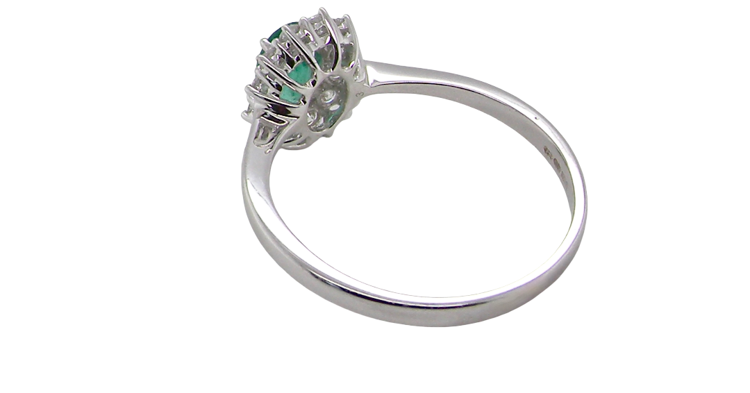 rear A classic cluster ring set with an oval cut emerald centre stone, measures 6x4mm, grass green colour.
Complimented by an outer halo of twelve brilliant cut white diamonds, each 1.7mm (total est at 0.25 carats)