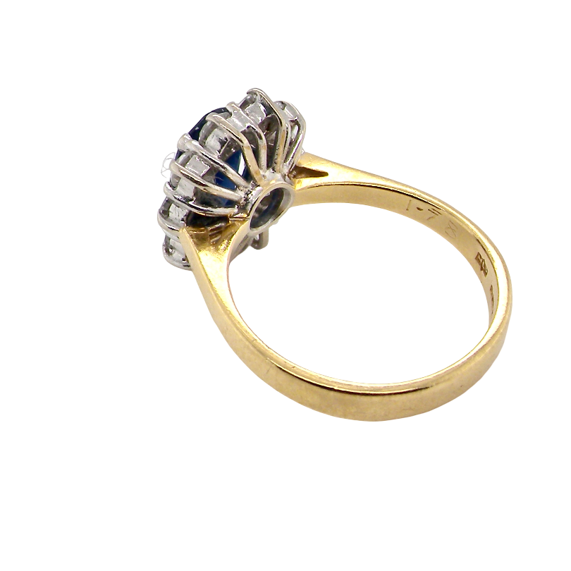 A vintage-style ring with a yellow gold band and a silver-toned floral cluster setting featuring dark blue and clear stones, shown on a plain white background.