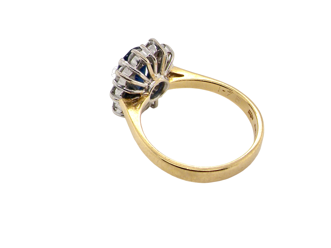 A vintage-style ring with a yellow gold band and a silver-toned floral cluster setting featuring dark blue and clear stones, shown on a plain white background.