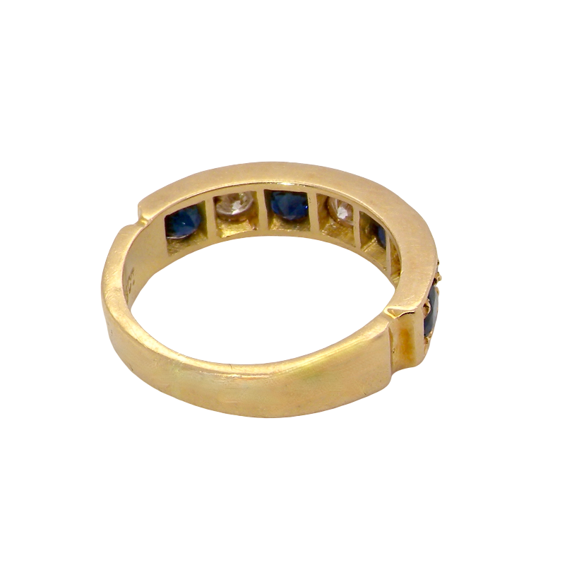A vintage gold ring with a split shank design, featuring rows of dark blue round sapphires and a central clear stone, shown on a plain white background.