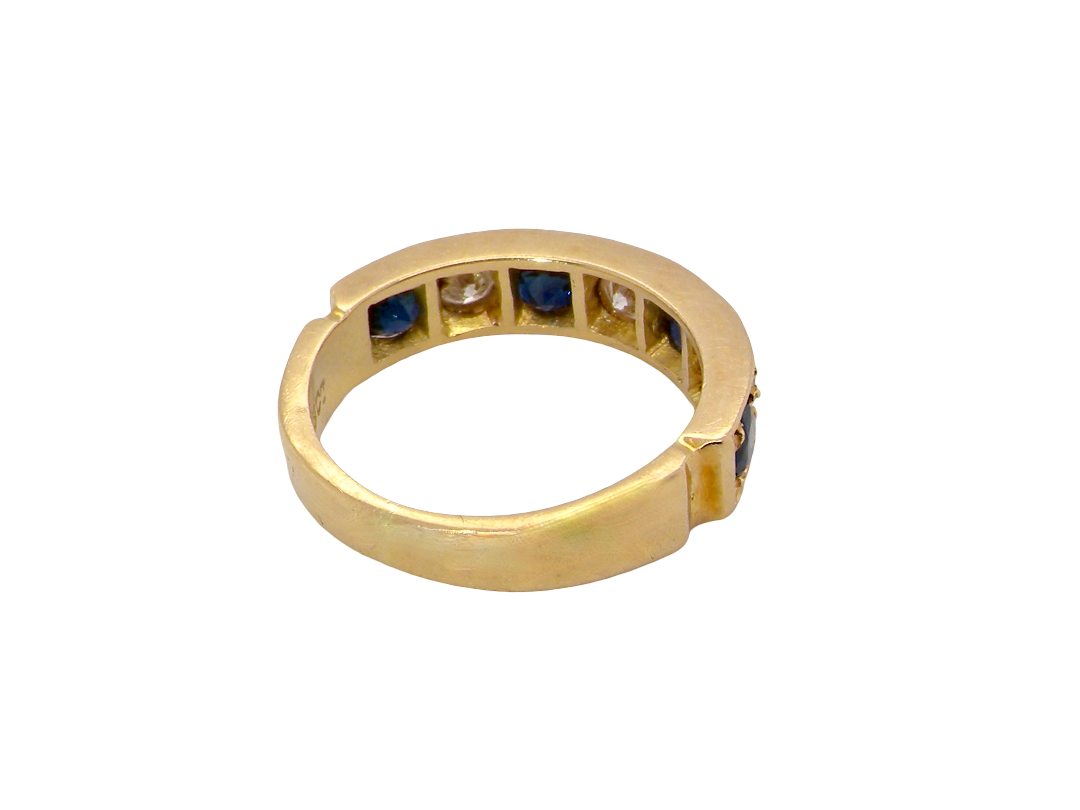 A vintage gold ring with a split shank design, featuring rows of dark blue round sapphires and a central clear stone, shown on a plain white background.