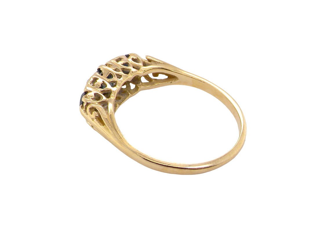A yellow gold ring with an intricate filigree crown featuring small dark blue gemstones, shown on a plain white background.