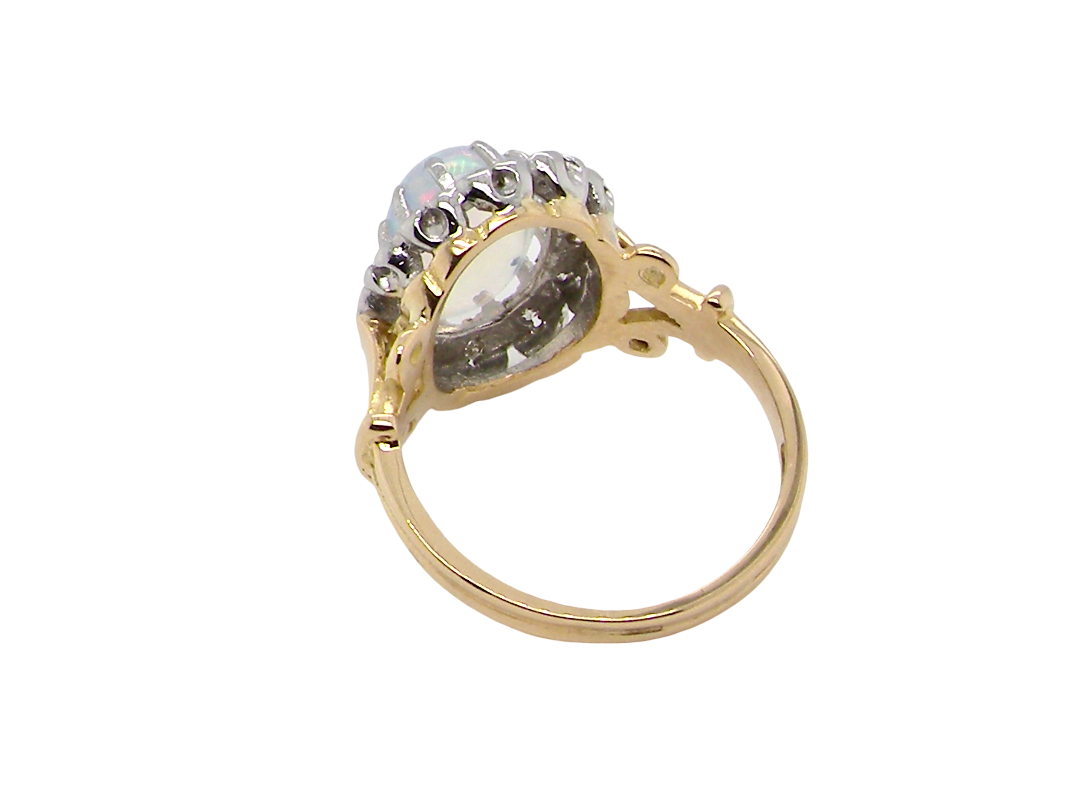 rear An 18 carat gold cluster ring. Features an oval opal centre stone with excellent play of colour with a predominance of watery purple and flashes of orange, and luminous green.
Measures 11x7mm.
