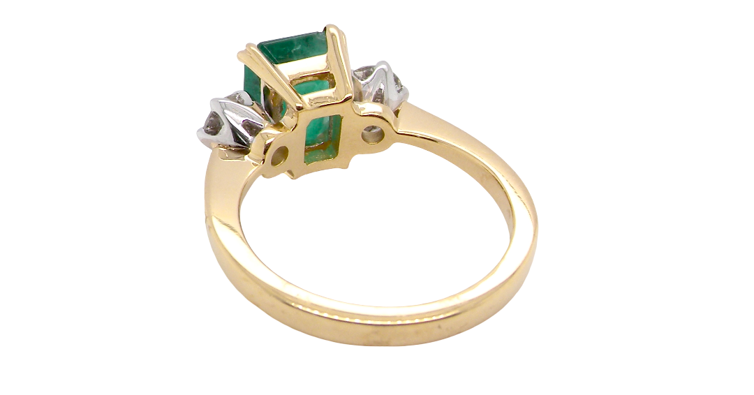 rear An exceptional three-stone ring featuring a vibrant step-cut emerald to the centre, measuring 8.6 x 7.0mm and weighing approximately 2.10 carats. The emerald displays a beautiful grass-green colour and is secured in a classic four-claw setting.