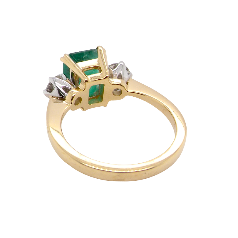 rear An exceptional three-stone ring featuring a vibrant step-cut emerald to the centre, measuring 8.6 x 7.0mm and weighing approximately 2.10 carats. The emerald displays a beautiful grass-green colour and is secured in a classic four-claw setting.