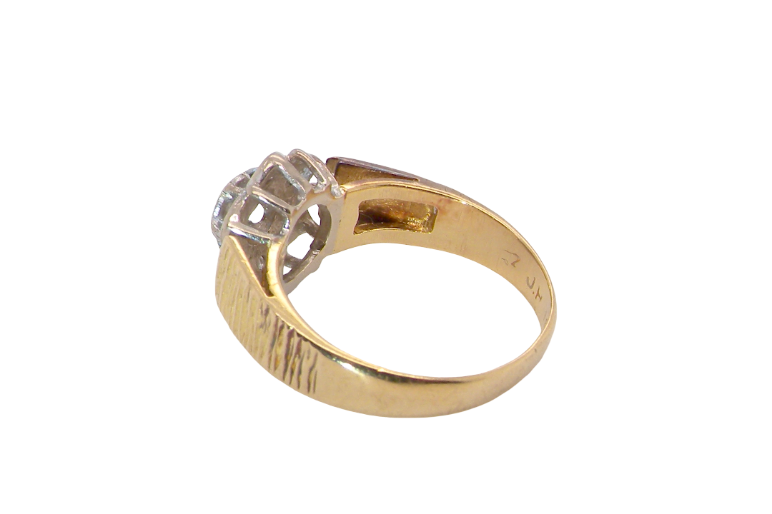 rear typical design from the 1960s/1970s era, a daisy cluster set with brilliant cut white diamonds and and a bark design finish to both shoulders.
Central diamond measures 2.5mm, and an outer halo of six more diamonds, at 1.2mm each and illusion set in white gold. (Total est carat weight 0.15 carats). Head measures 10mm. The band and shoulders test as 18 carat gold. 