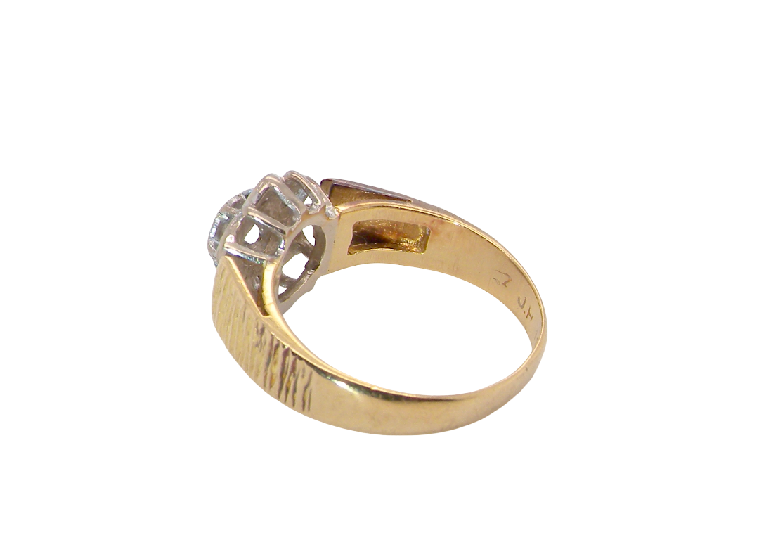 rear typical design from the 1960s/1970s era, a daisy cluster set with brilliant cut white diamonds and and a bark design finish to both shoulders.
Central diamond measures 2.5mm, and an outer halo of six more diamonds, at 1.2mm each and illusion set in white gold. (Total est carat weight 0.15 carats). Head measures 10mm. The band and shoulders test as 18 carat gold. 