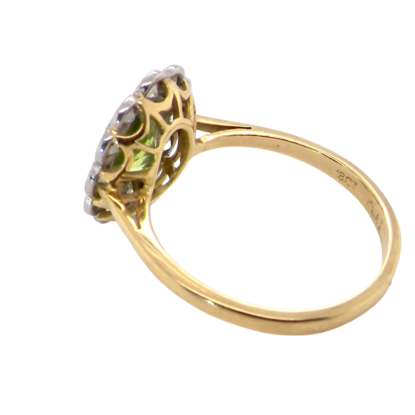 A yellow gold ring with a decorative cluster setting featuring small clear stones and a central green gemstone, shown on a plain white background.