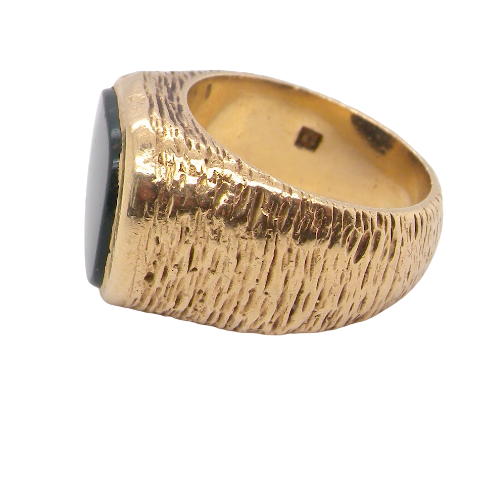 Gold ring with a textured band and black gemstone on a white background