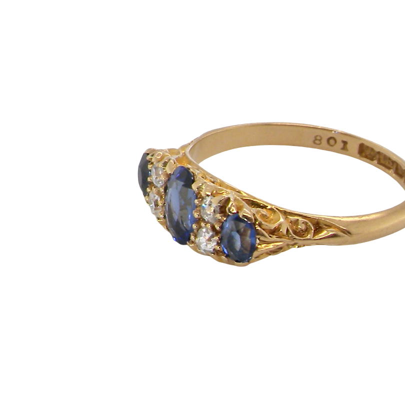 A vintage-style yellow gold ring featuring three oval-cut deep blue sapphires and small clear accent stones, shown on a plain white background. The inner band is stamped with '807'.