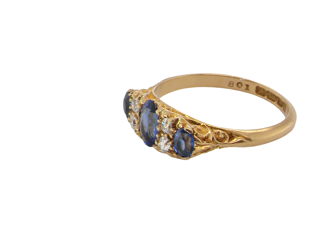 A vintage-style yellow gold ring featuring three oval-cut deep blue sapphires and small clear accent stones, shown on a plain white background. The inner band is stamped with '807'.