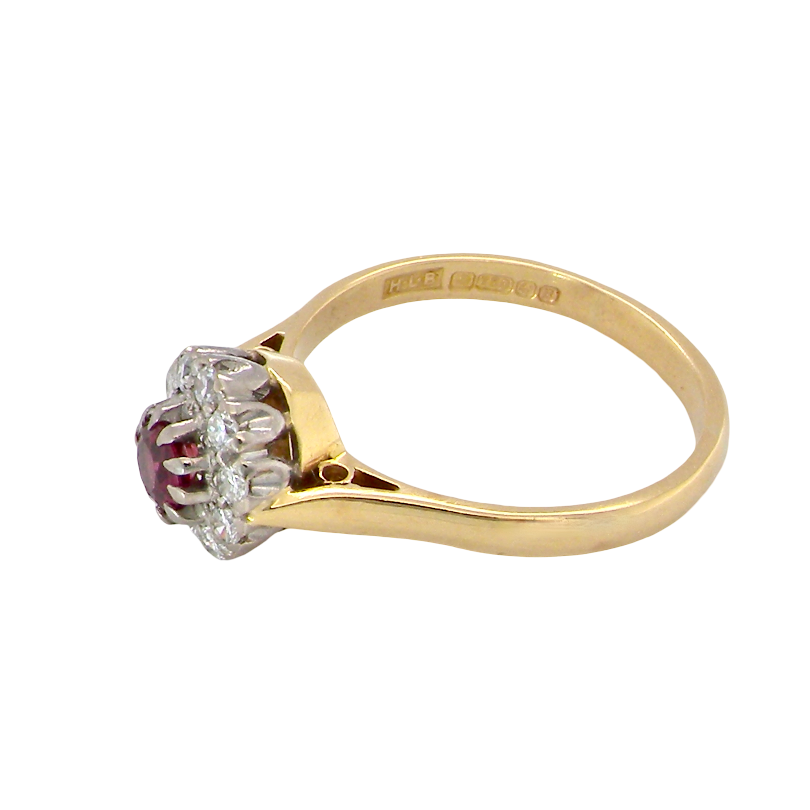 A vintage yellow gold ring with a central cluster of clear stones and a round red ruby gemstone, shown on a plain white background.