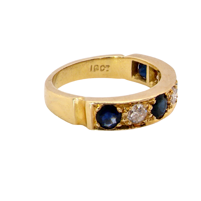 A vintage yellow gold ring featuring round blue sapphires and a central clear diamond, shown on a plain white background. The inside of the band is stamped with '18CT'.