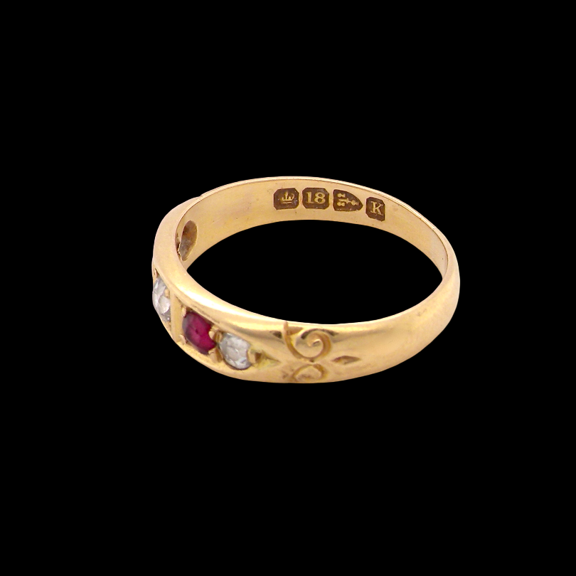 A vintage yellow gold ring with floral engravings and small gemstone accents, shown on a solid black background.