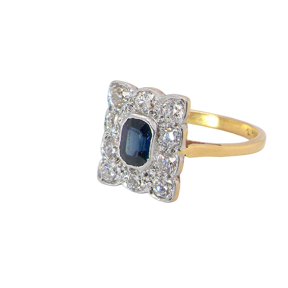 side A rectangular cluster ring that features in its centre a cushion shaped dark blue sapphire, that measures 5x3.5mm (est 0.30 carats)