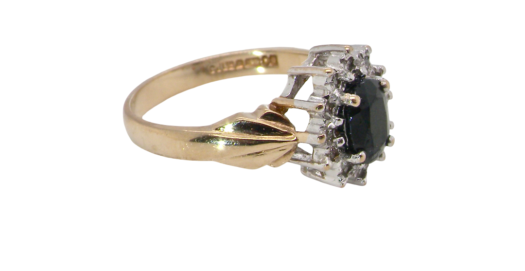 side A traditional cluster ring that features to the centre a dark black blue oval cut sapphire 7x5mm (est 3/4 ct) claw set.