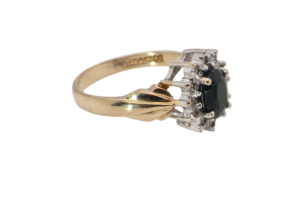 side A traditional cluster ring that features to the centre a dark black blue oval cut sapphire 7x5mm (est 3/4 ct) claw set.