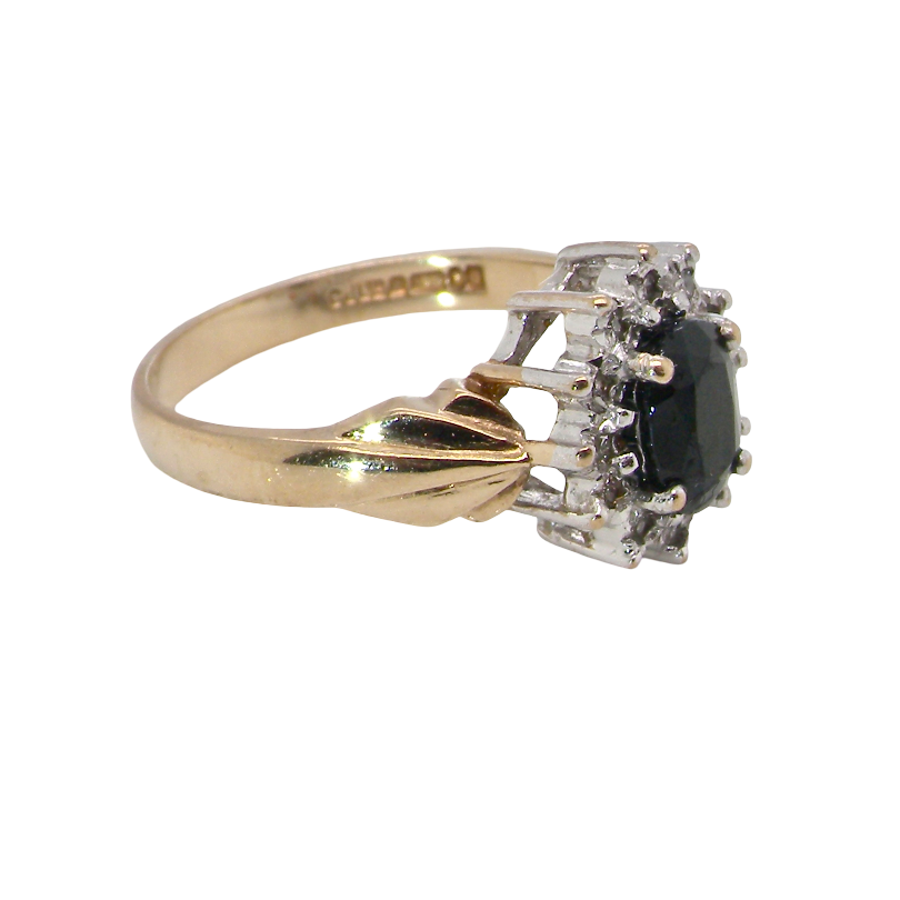 side A traditional cluster ring that features to the centre a dark black blue oval cut sapphire 7x5mm (est 3/4 ct) claw set.