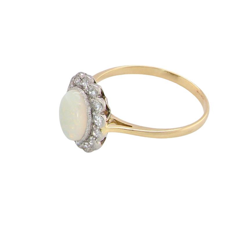 A yellow gold ring featuring a round white opal center stone surrounded by a halo of small clear stones, set on a plain white background.