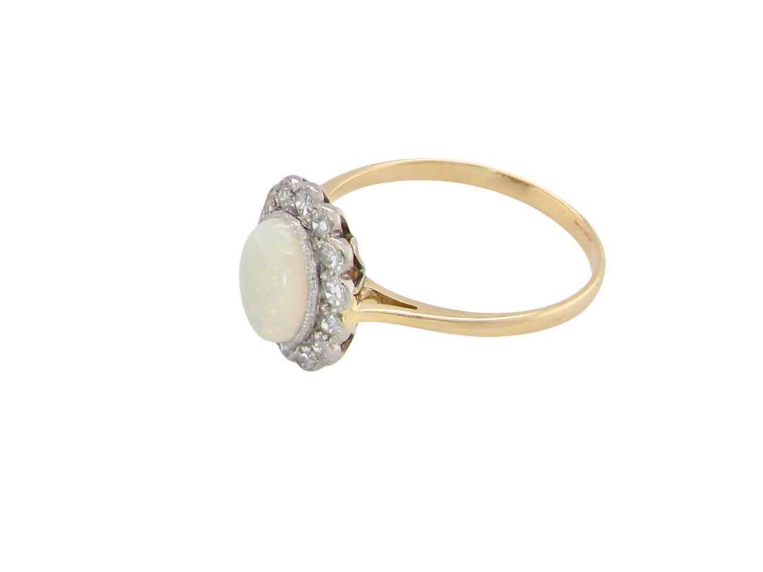 A yellow gold ring featuring a round white opal center stone surrounded by a halo of small clear stones, set on a plain white background.