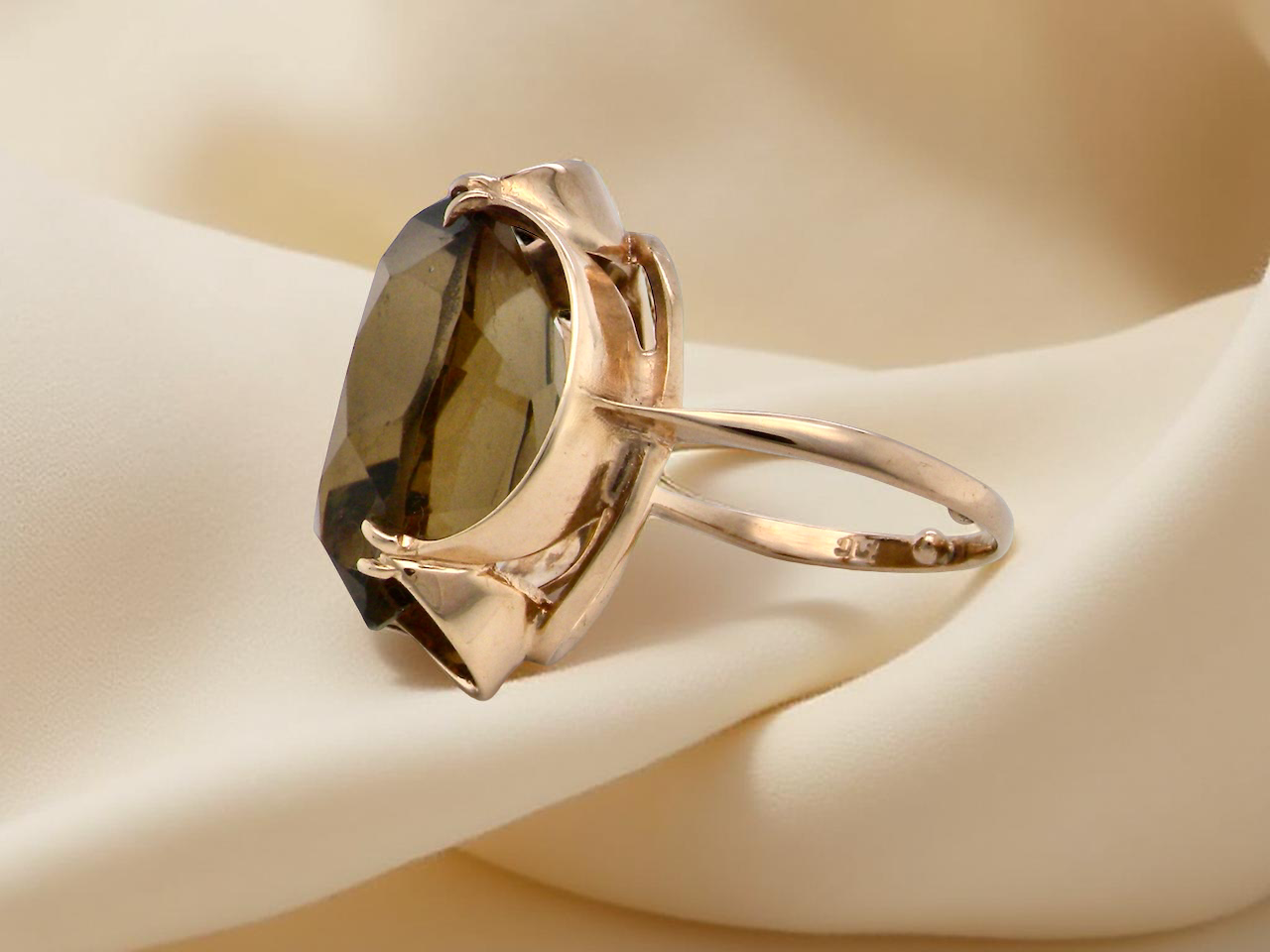 Gold ring with a large brown gemstone on a beige background