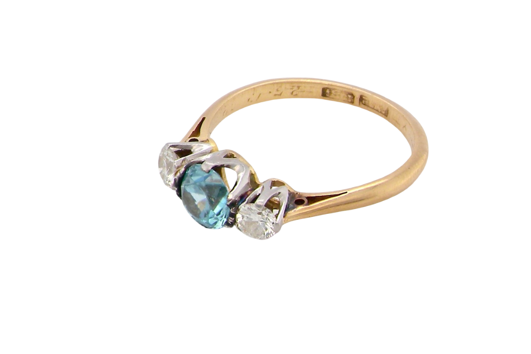 side A vintage three stone ring. Centre stone, a round 5.8mm natural blue zircon.
To each side an old brilliant cut white diamond 4mm round (est 0.25 carats). Colour i-j, clarity Si.