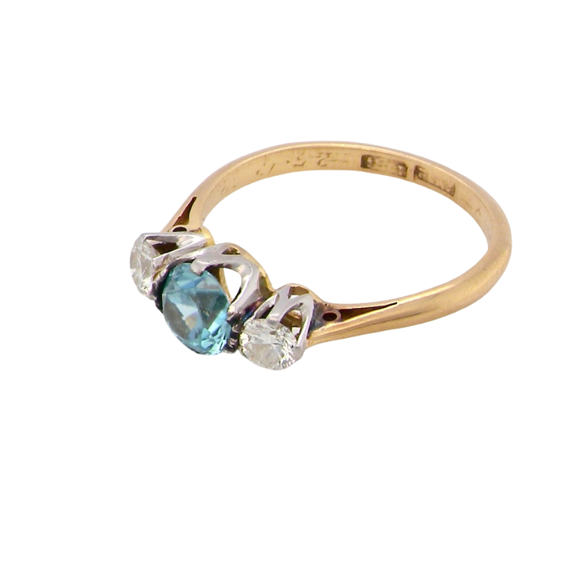 side A vintage three stone ring. Centre stone, a round 5.8mm natural blue zircon.
To each side an old brilliant cut white diamond 4mm round (est 0.25 carats). Colour i-j, clarity Si.