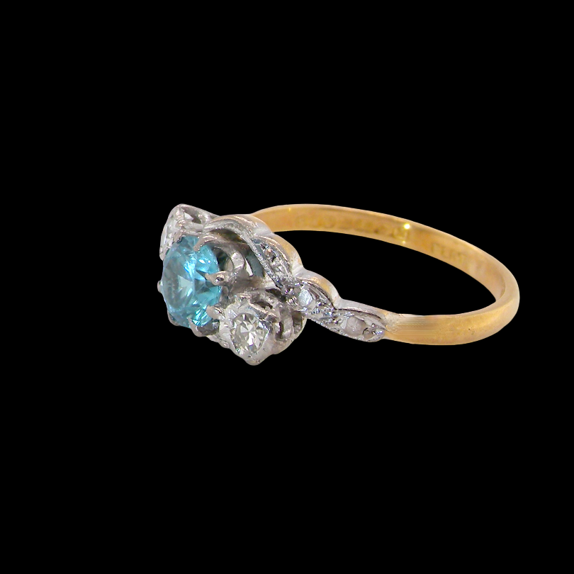 side A vintage three stone ring, cross over style and features a round 6mm natural blue zircon centre stone