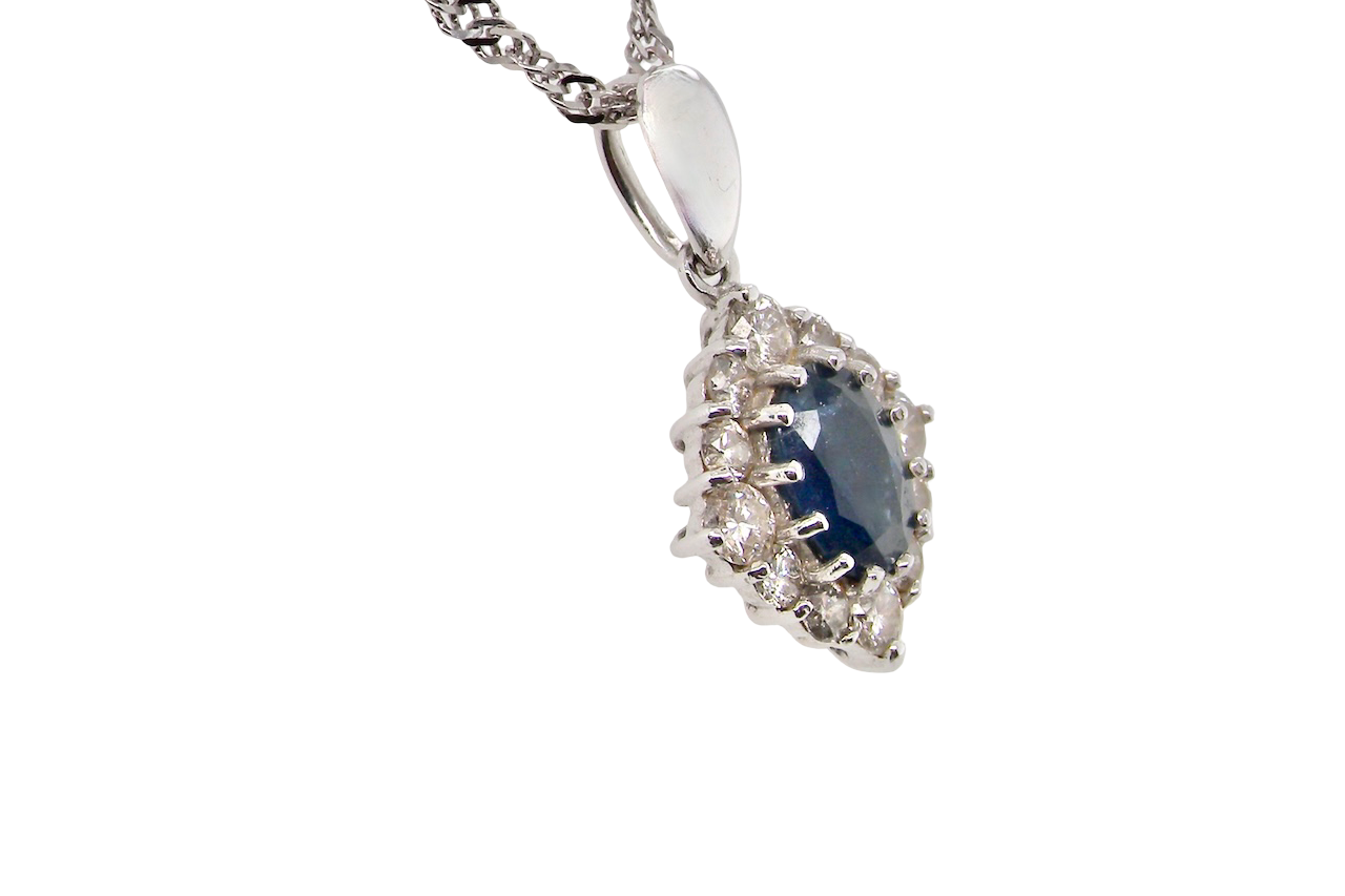 side A white gold pendant. The centre stone an inky black blue sapphire 7x5mm, claw set. Complimented by an outer halo of twelve brilliant cut white diamonds.
