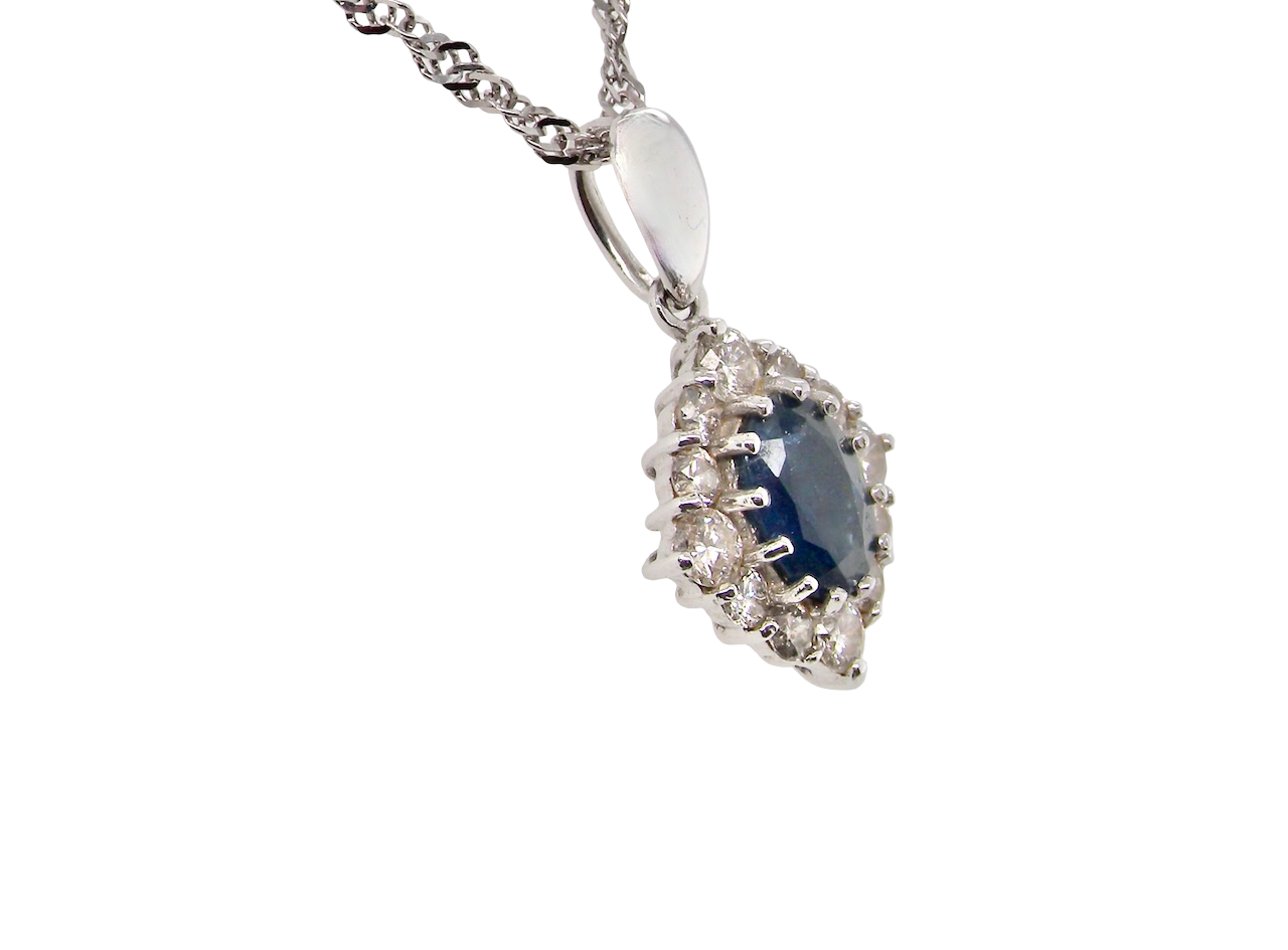 side A white gold pendant. The centre stone an inky black blue sapphire 7x5mm, claw set. Complimented by an outer halo of twelve brilliant cut white diamonds.