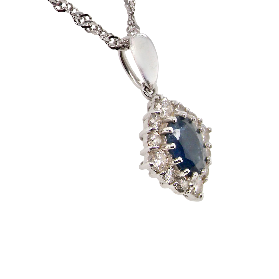 side A white gold pendant. The centre stone an inky black blue sapphire 7x5mm, claw set. Complimented by an outer halo of twelve brilliant cut white diamonds.