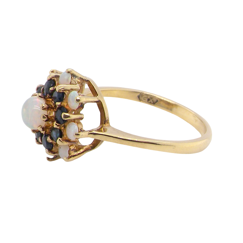 A vintage-style gold ring featuring a cluster of white opal gemstones and small dark blue stones, set on a polished yellow gold band against a plain white background.