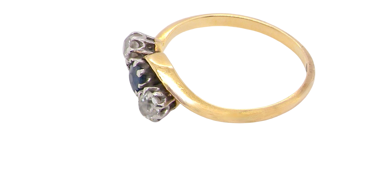side An 18 carat gold three stone cross over ring.
Centre stone a round sapphire 4mm diameter. Each side a brilliant cut white diamond 4mm diameter (0.25 carats estimated), colour i-k, clarity Si.