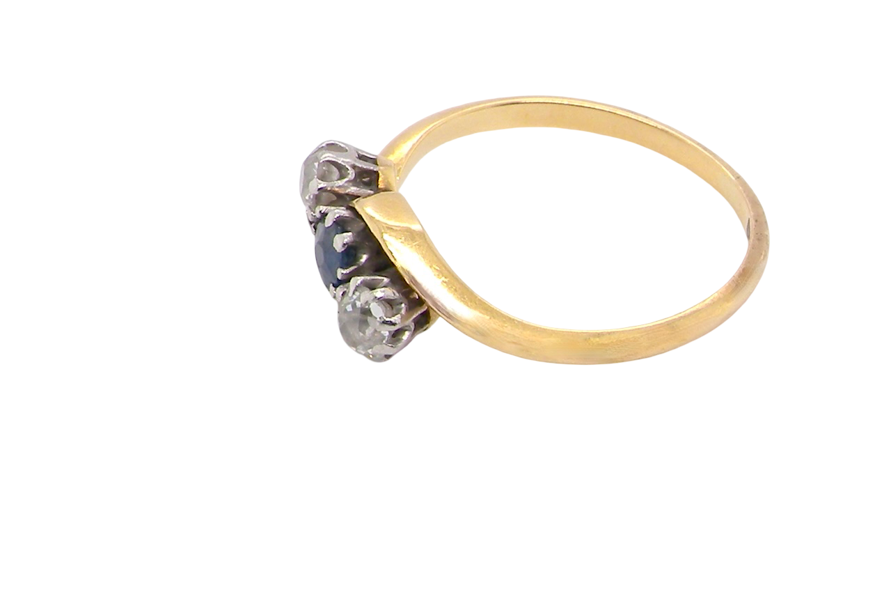 side An 18 carat gold three stone cross over ring.
Centre stone a round sapphire 4mm diameter. Each side a brilliant cut white diamond 4mm diameter (0.25 carats estimated), colour i-k, clarity Si.